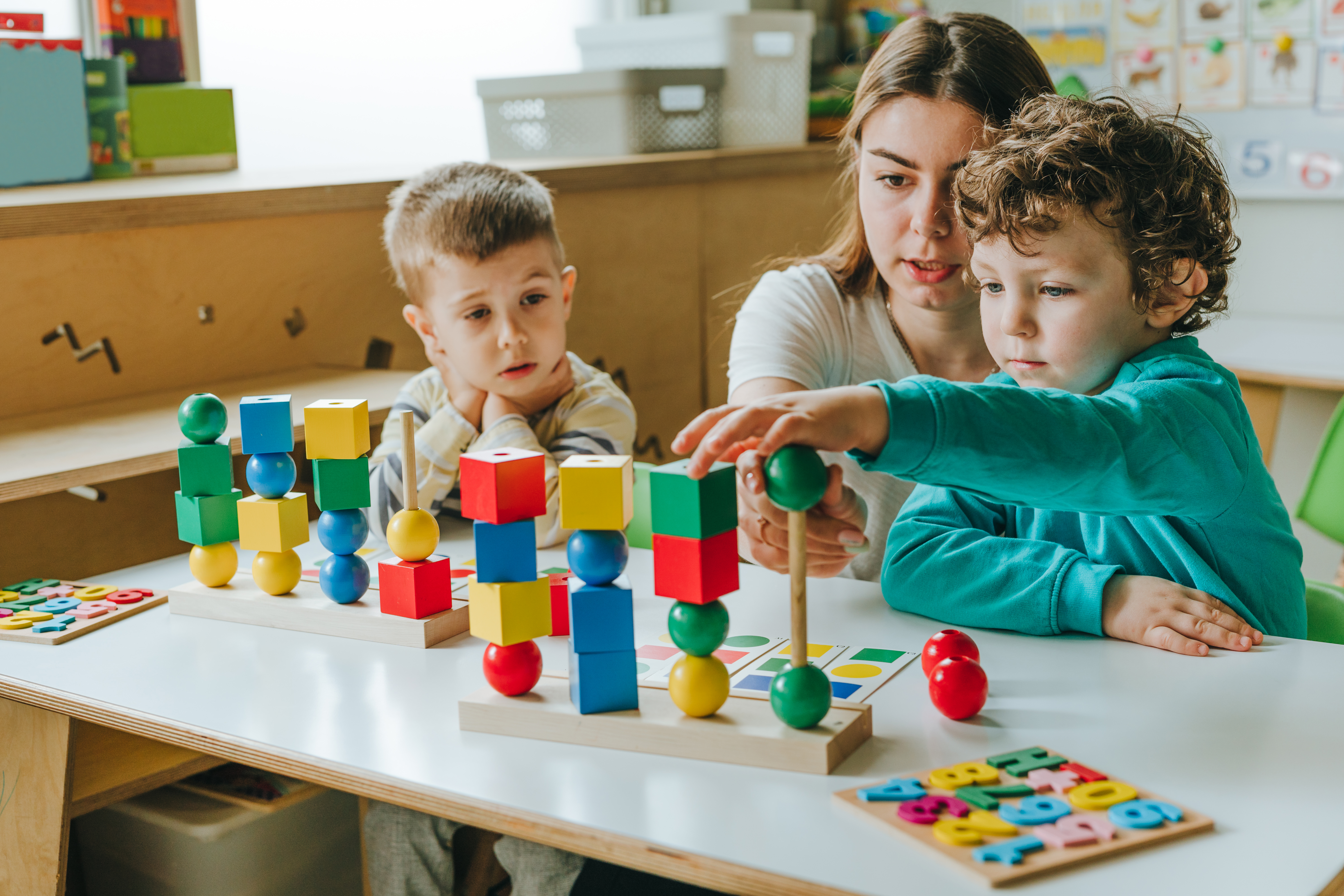 Female teacher helping little boy sorting blocks by color in a kindergarten. Early development concept. Selective focus.