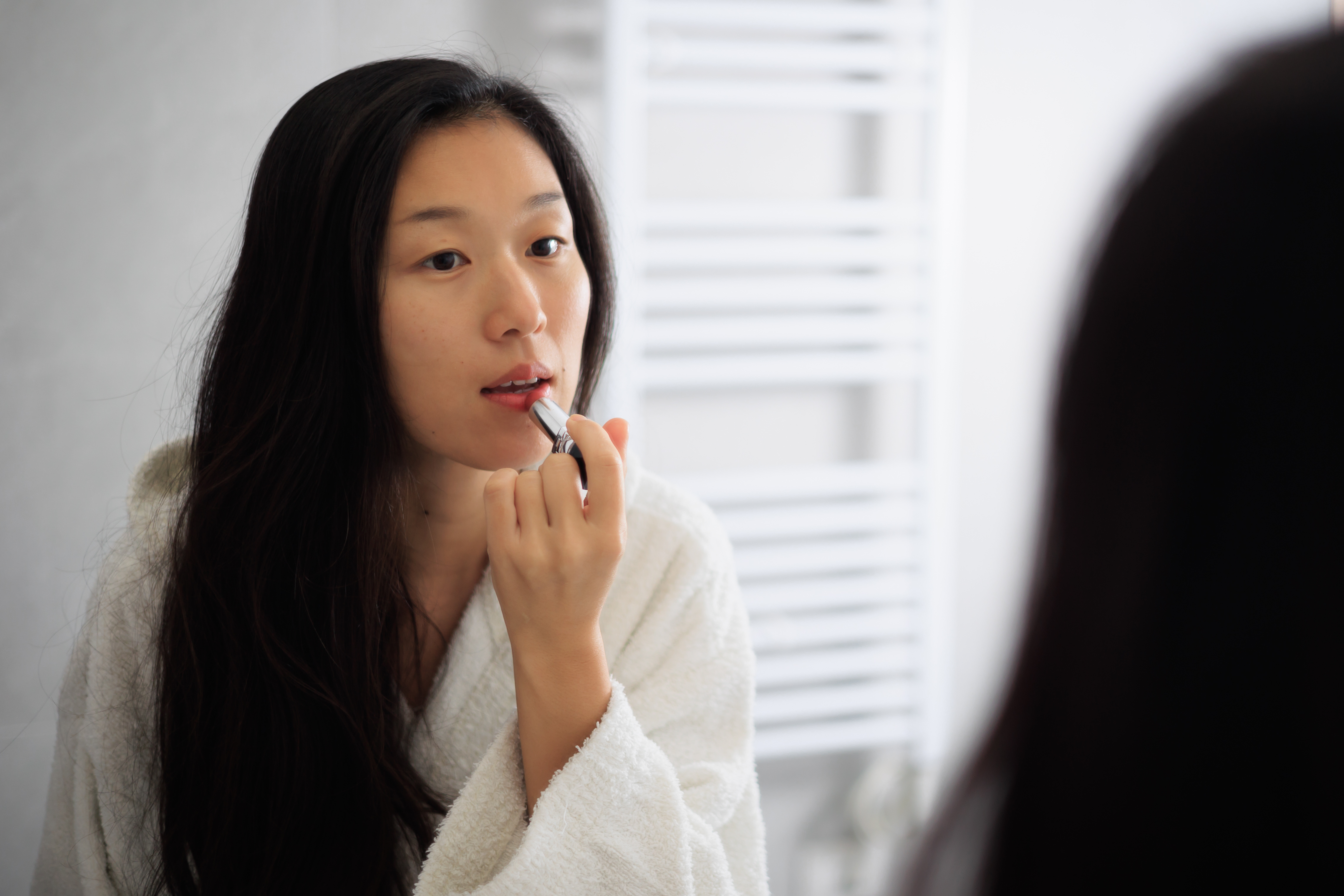 Asian lady in bathroom mirror after shower, applying lipstick