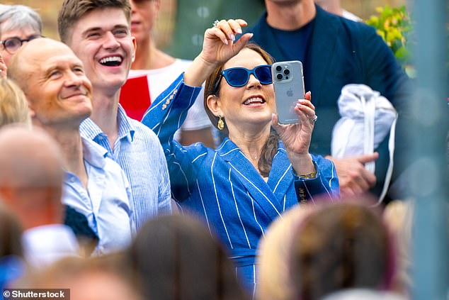 Queen Mary of Denmark takes photos of her son Crown Prince Christian as he sprays champagne from a party bus to celebrate his high school graduation