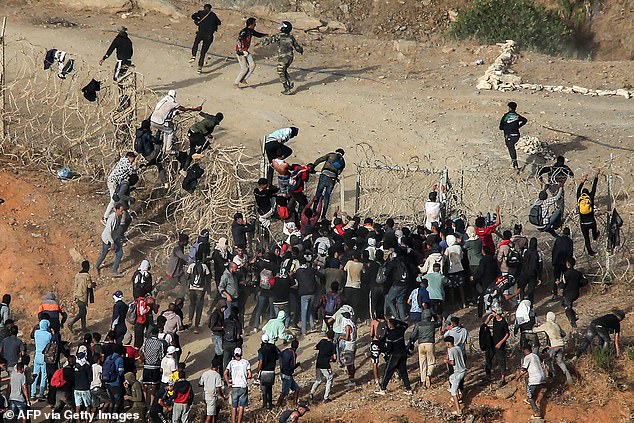 Migrants storm EU border: Hundreds of people swarm over barbed wire fences after throwing rocks at Moroccan guards following calls on social media to force their way into the Spanish enclave