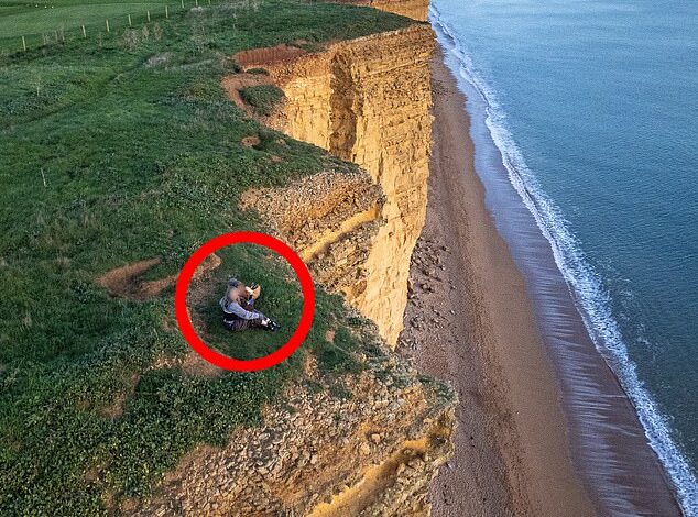 The height of stupidity! Two women risk their lives as they sit on the edge of a crumbling 160-foot cliff and watch the sunset, just weeks after the great rockfall